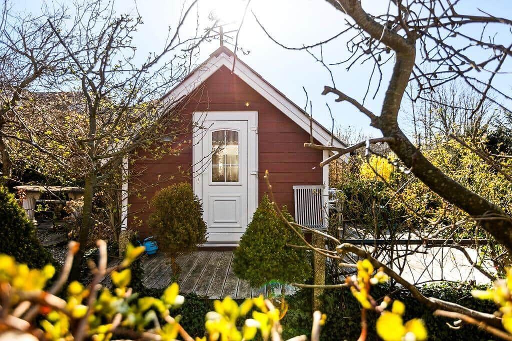 Rotes Holzhaus mit weißer Tür und kleinen Garten.