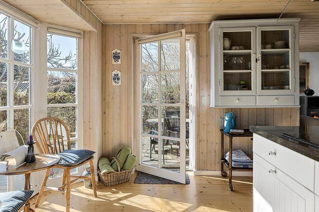 Raum mit Holzwänden, Fenstern und offener Tür zum Balkon.