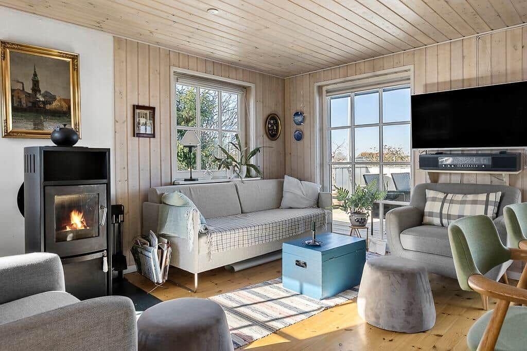 Wohnzimmer mit Kamin, Sofa, Sessel und TV. Holzwände und große Fenster.