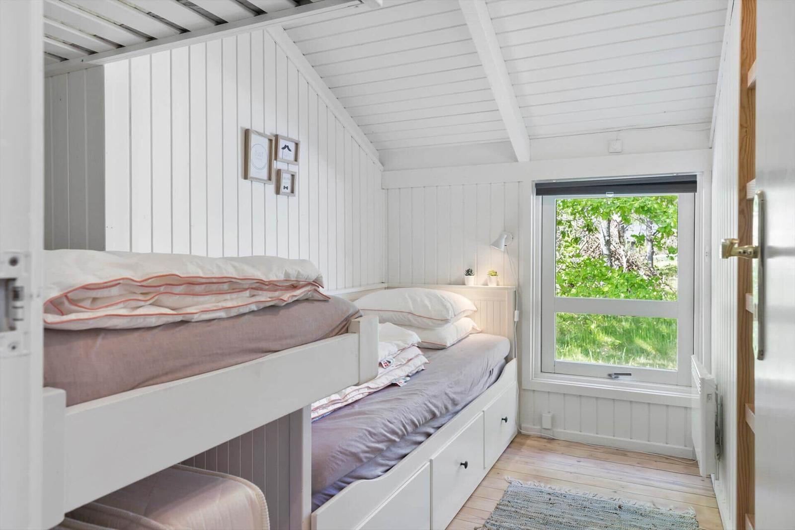 Zimmer mit Doppelstockbett, Fenster mit Blick auf Grün, weiß verkleidete Wände und Holzboden.