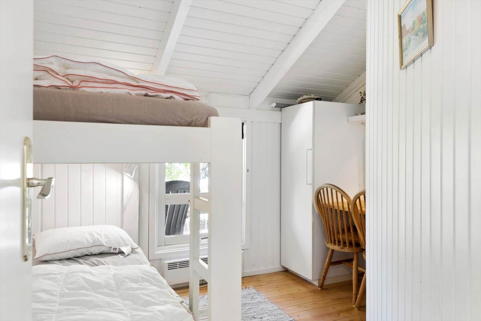 Zimmer mit Doppelstockbett, Schrank und Holzstühlen. Weiße Wände und Holzboden.