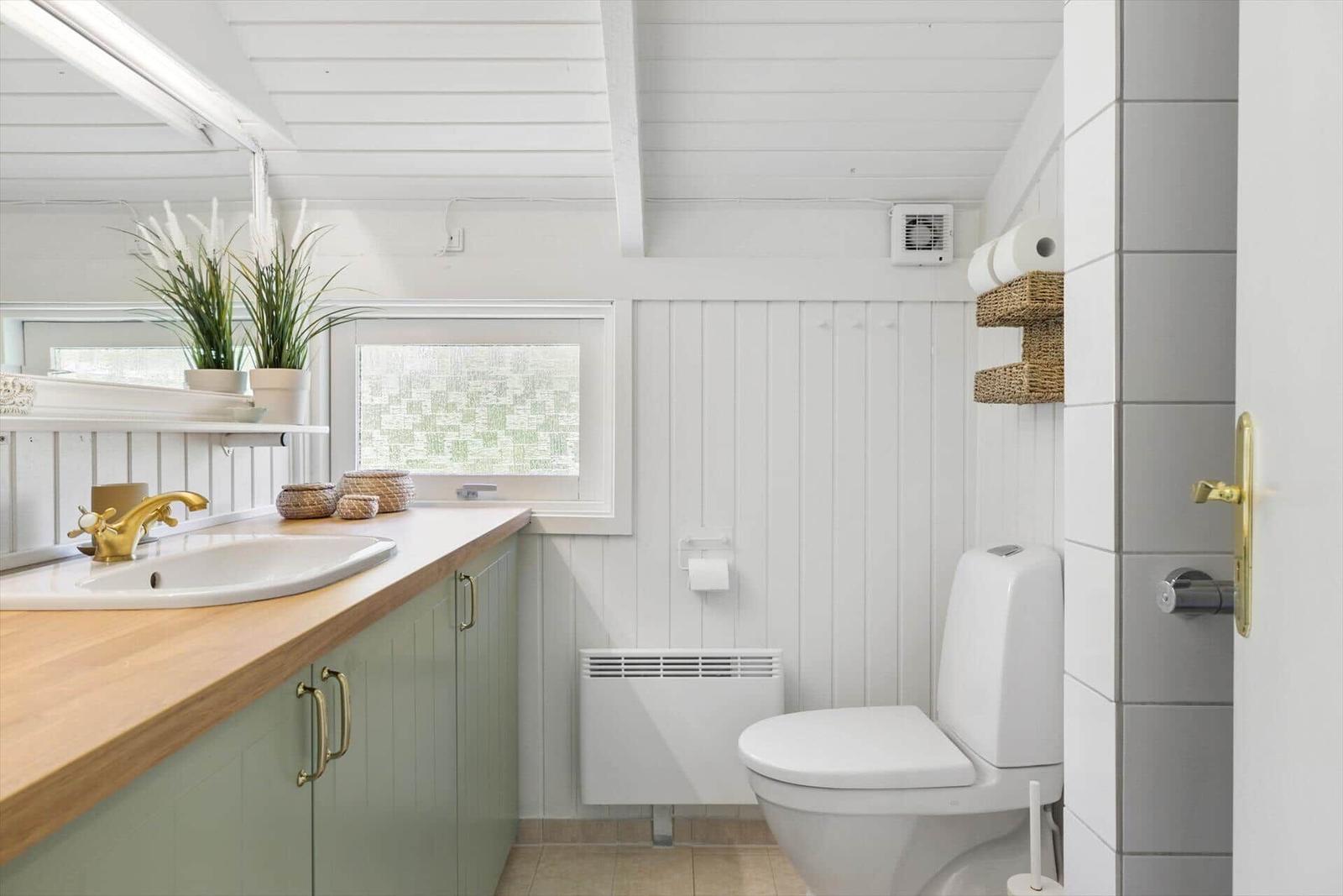 Badezimmer mit Waschbecken, Toilette und Fenster. Holzoberfläche und weiße Wände.