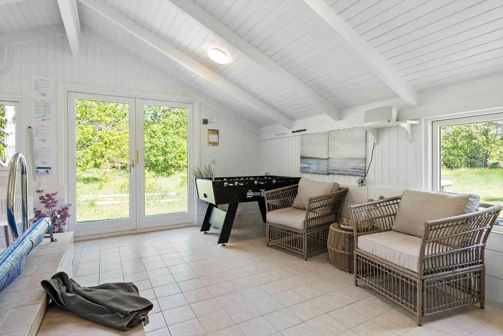Raum mit Foosballtisch, Rattanmöbeln und Glasfronten zur Außenterrasse.