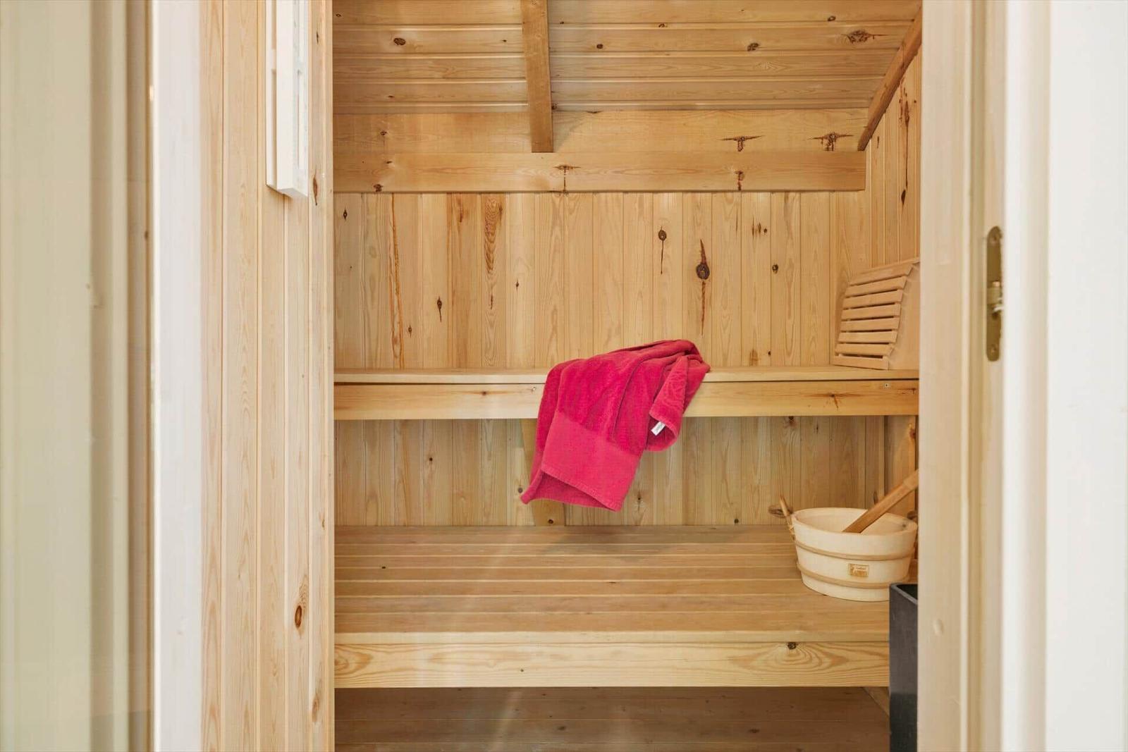 Holzsauna mit Bank, roter Handtuch und Eimer.