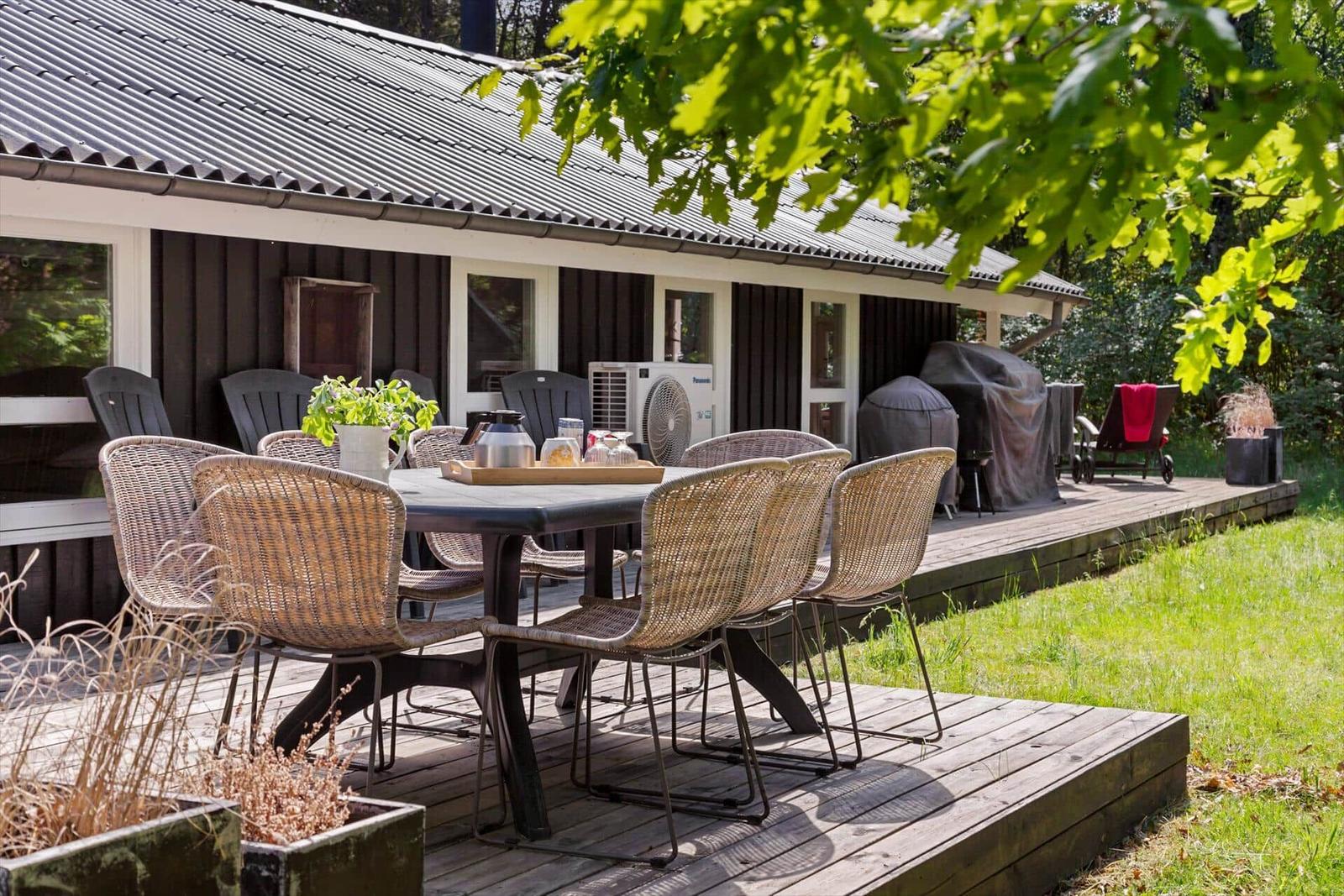 Terrasse mit Tisch und Stühlen, Grill und Gartenhaus im Hintergrund.