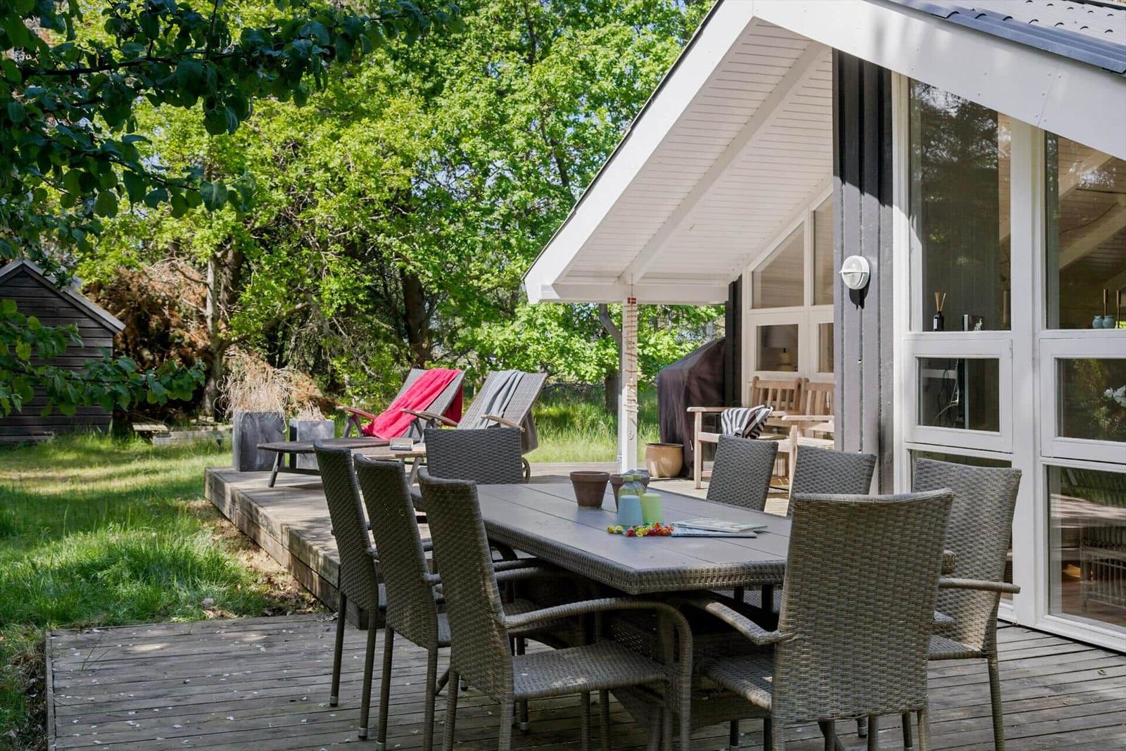 Terrasse mit Esstisch und Stühlen, umgeben von Grün und einem Haus.