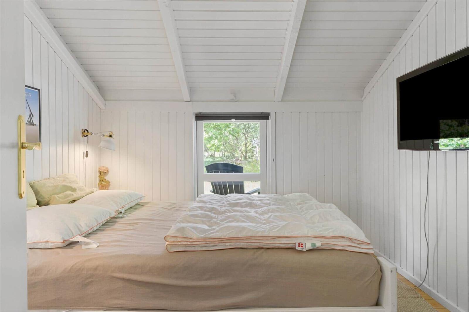 Schlafzimmer mit Bett, Fernseher und Fenster zum Garten.