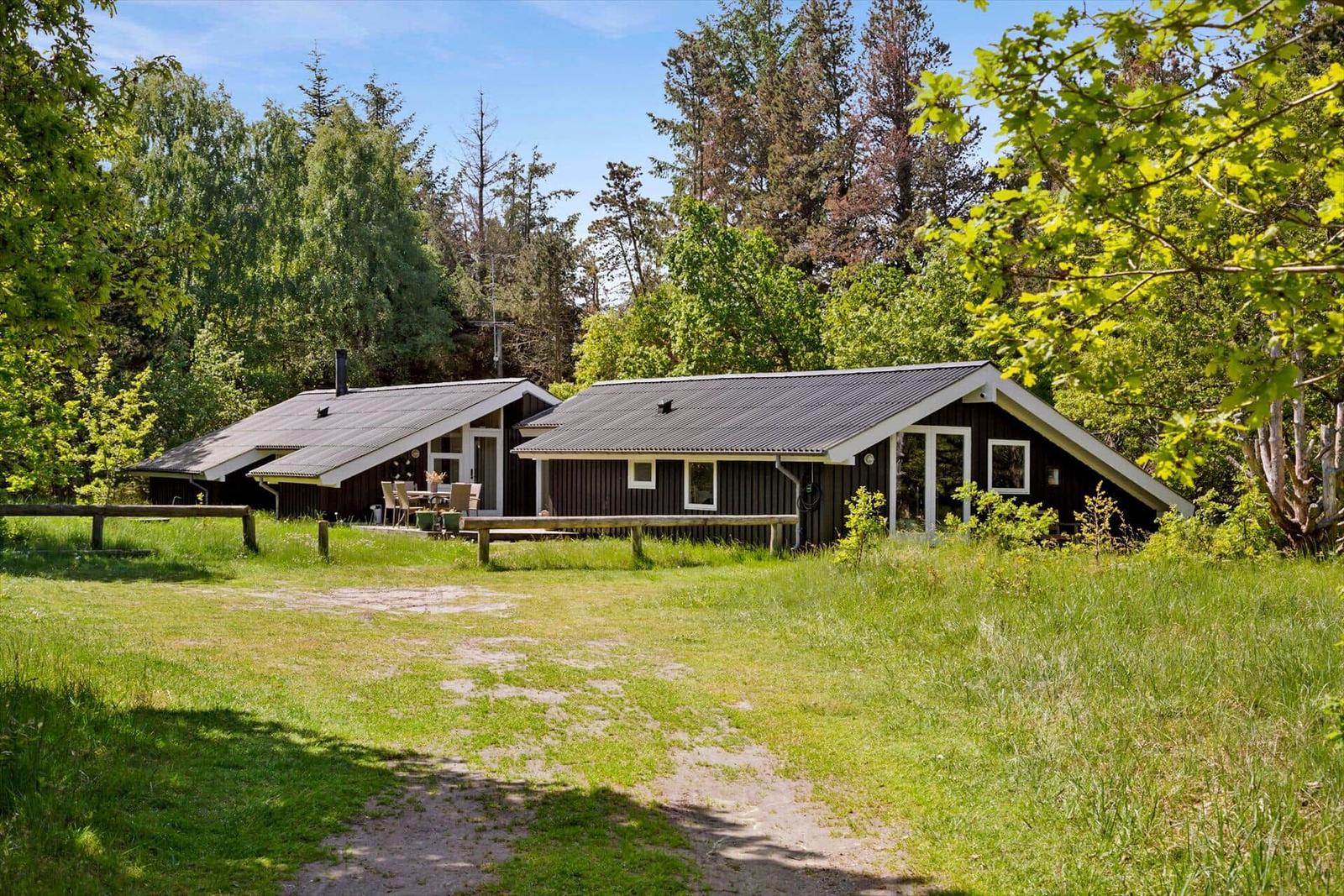 Zwei Holzhäuser mit Terrasse im Grünen. Grasfläche und Wald im Hintergrund.