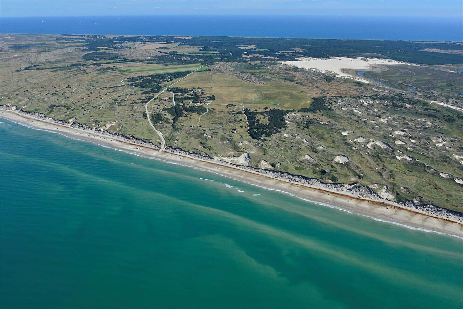 Aerielansicht einer Küstenlandschaft mit Strand, Dünen und Feldern.