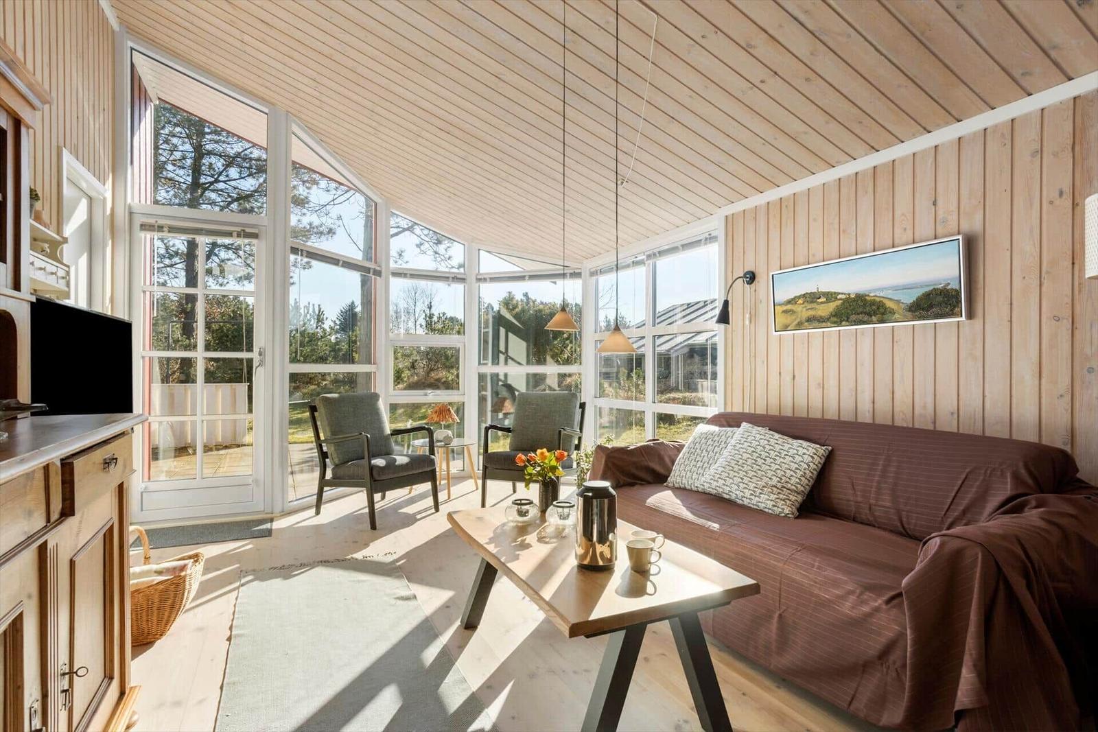 Wohnzimmer mit Holzwand, Sofa, Tisch und großem Fensterblick.