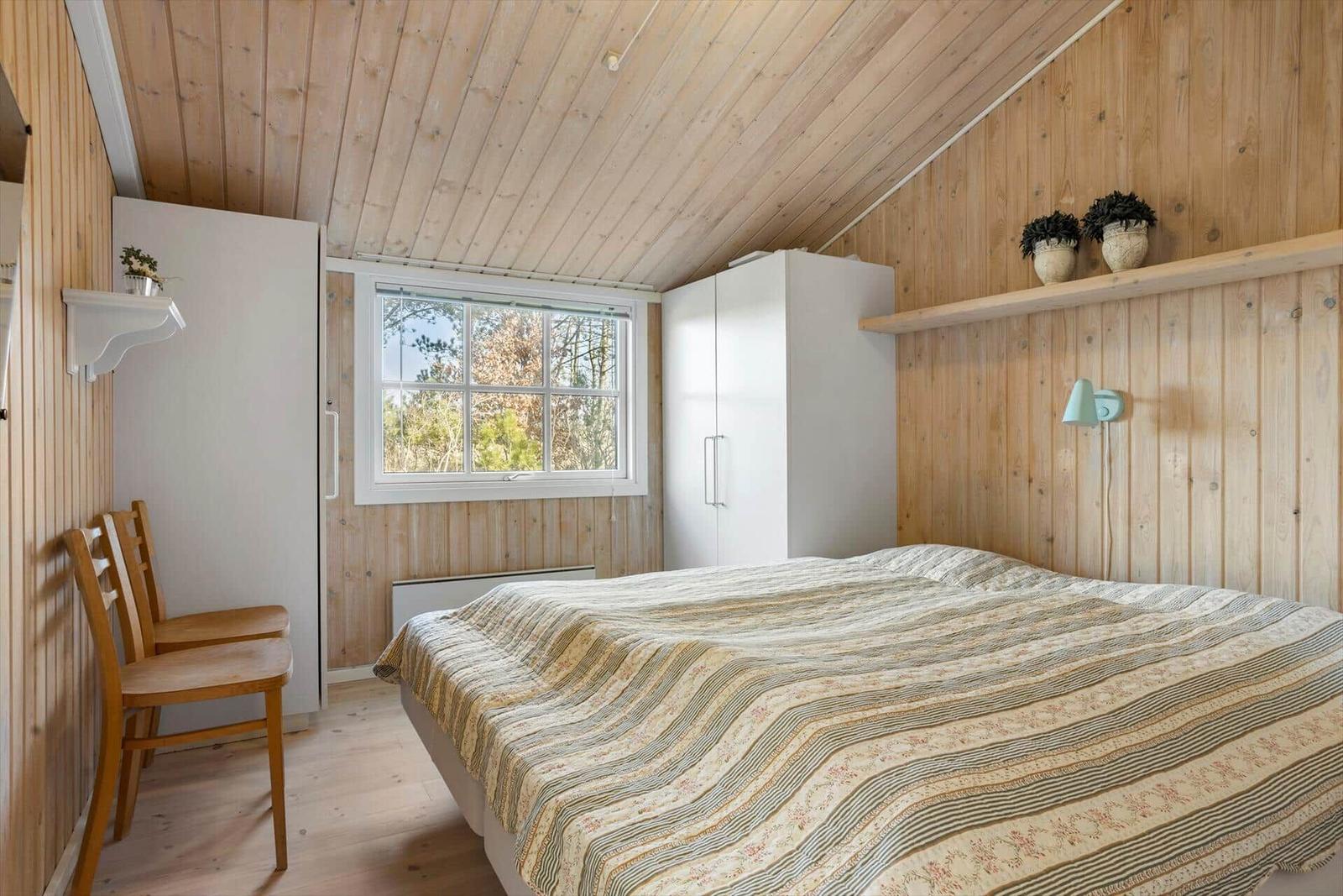 Schlafzimmer mit Holzwänden, Bett, Fenster und Schränken.