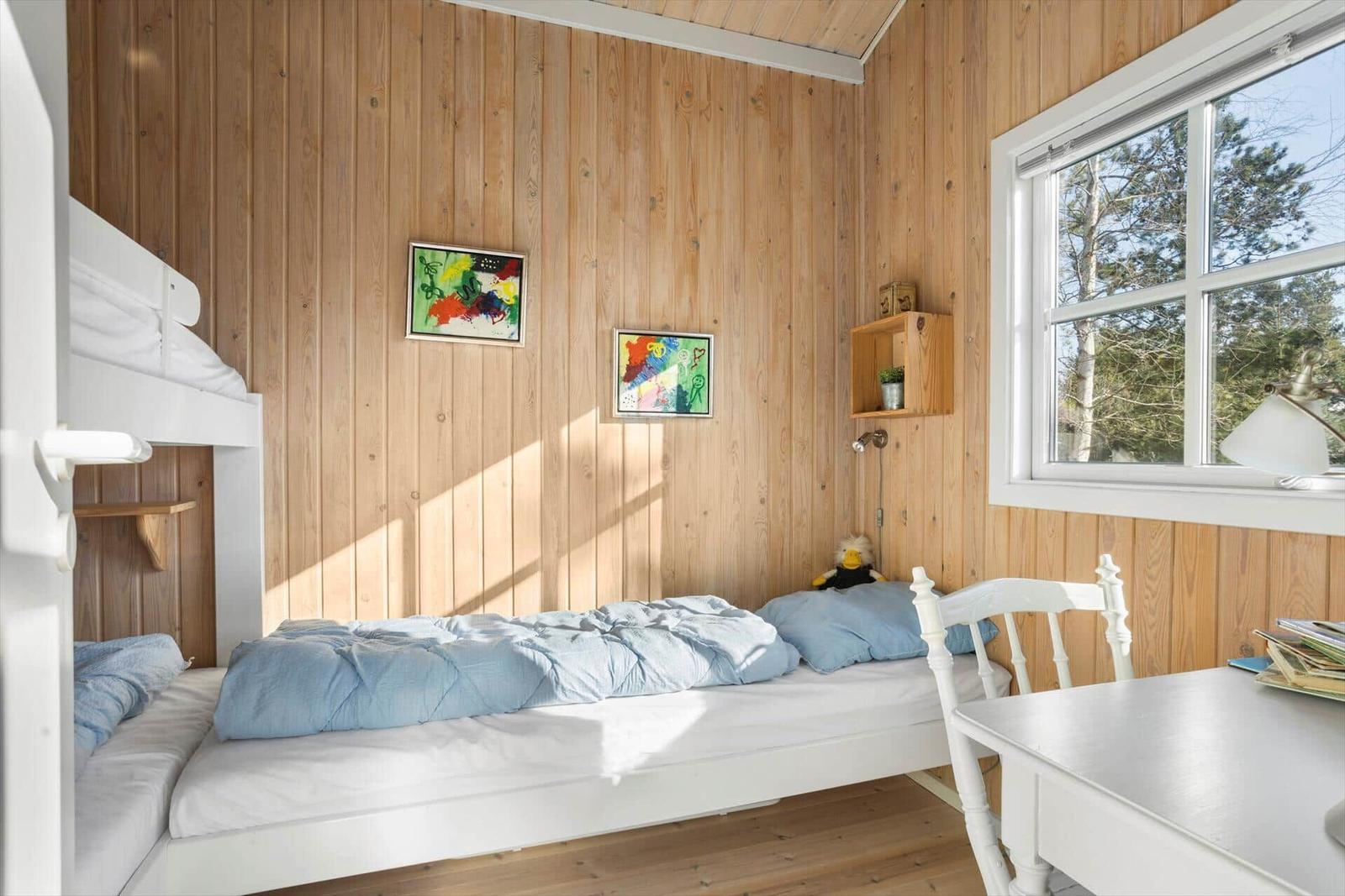 Schlafzimmer mit Doppelbett, Schreibtisch und Fenster mit Blick auf Bäume.