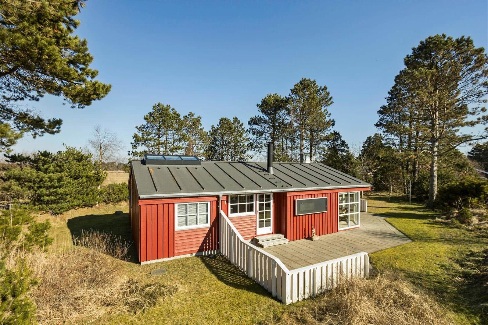 Rotes Holzhaus mit Terrasse und Schornstein zwischen Bäumen.