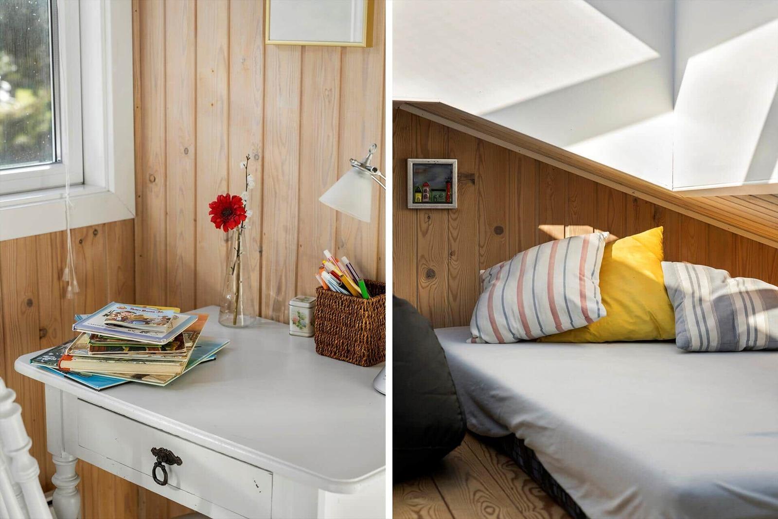 Schreibtisch mit Büchern und Blume neben einem Bett unter Dachschräge.