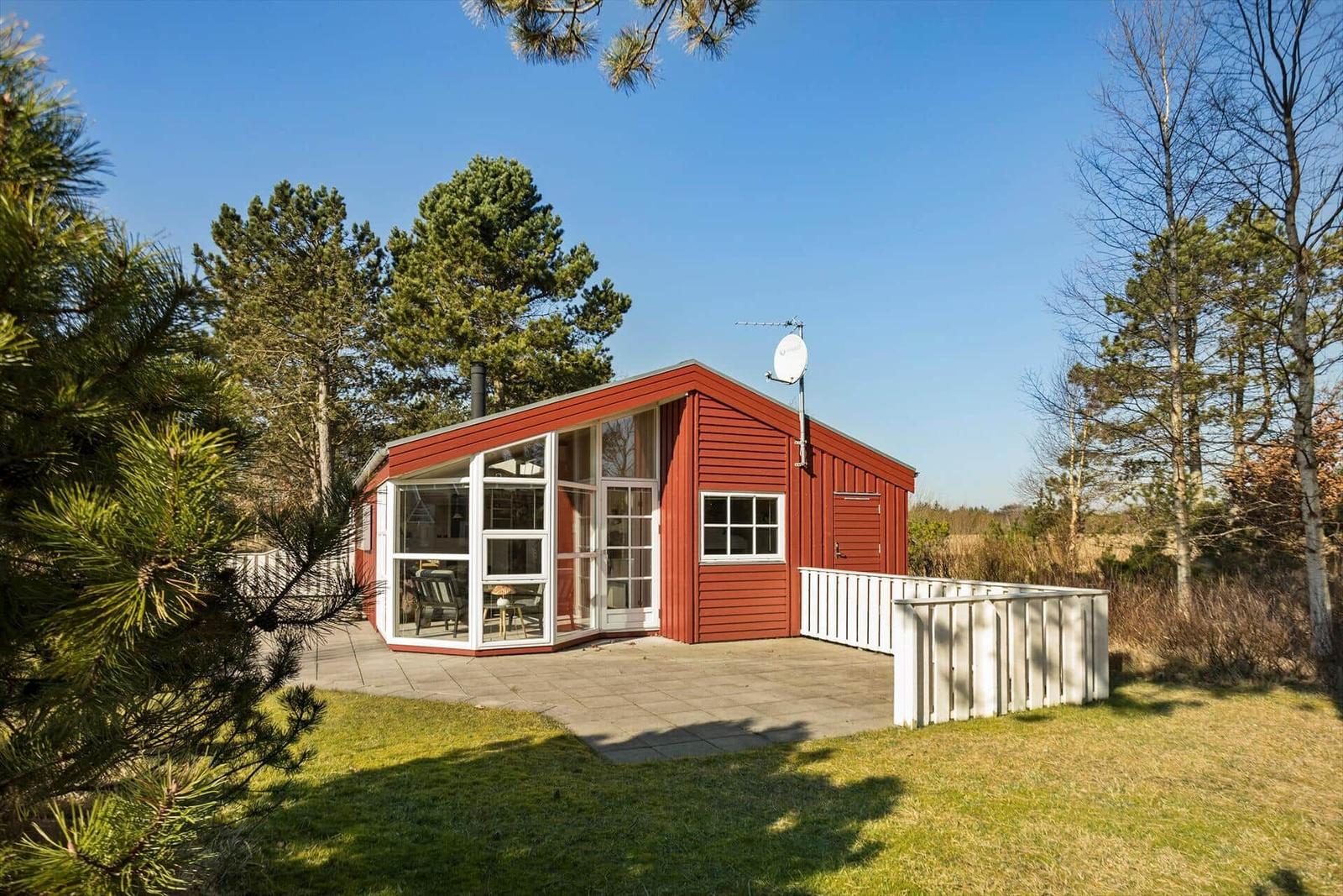 Rotes Holzhaus mit großem Fensterbereich und Terrasse in grüner Umgebung.