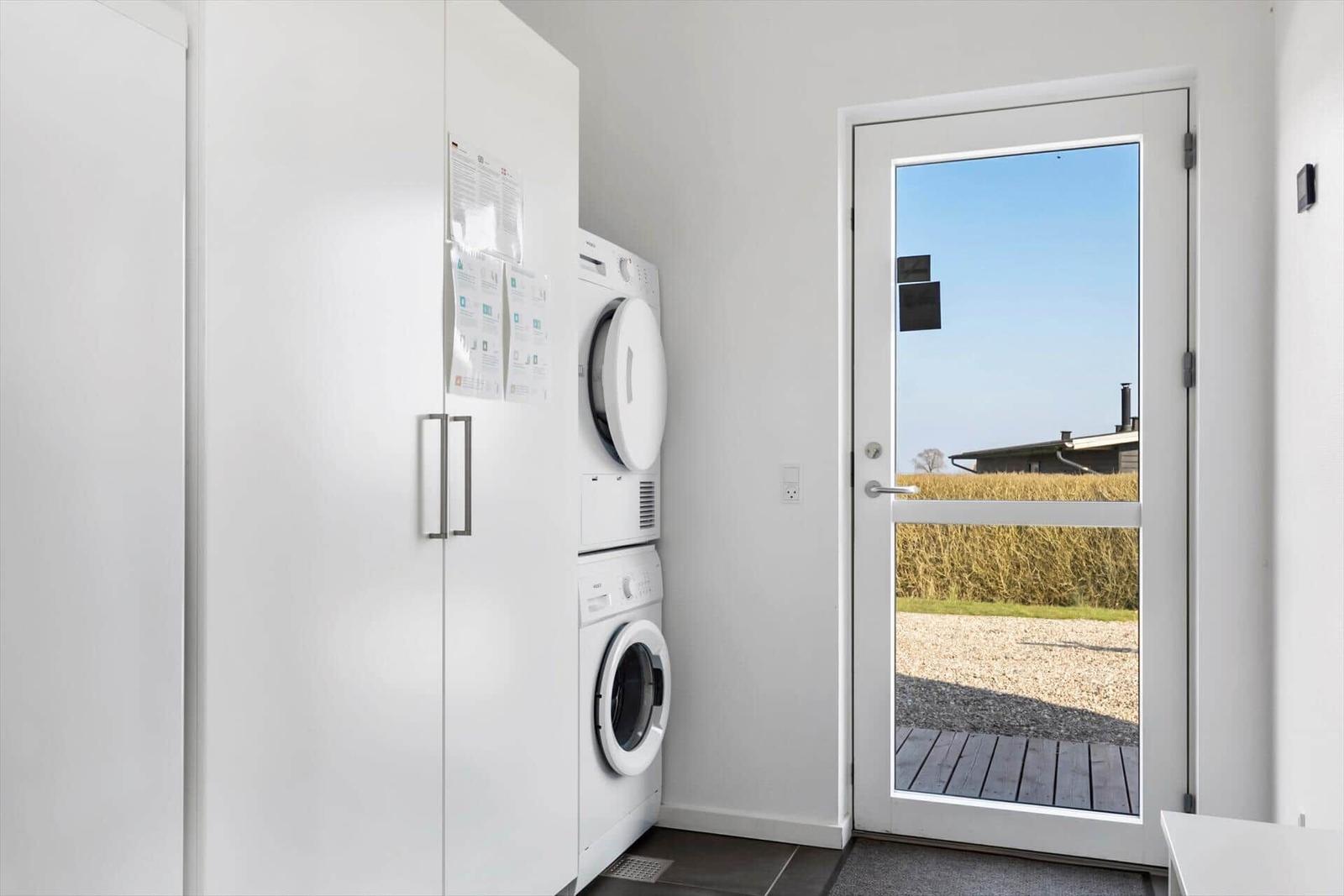 Washing machine and dryer next to a door with view of a terrace and field.