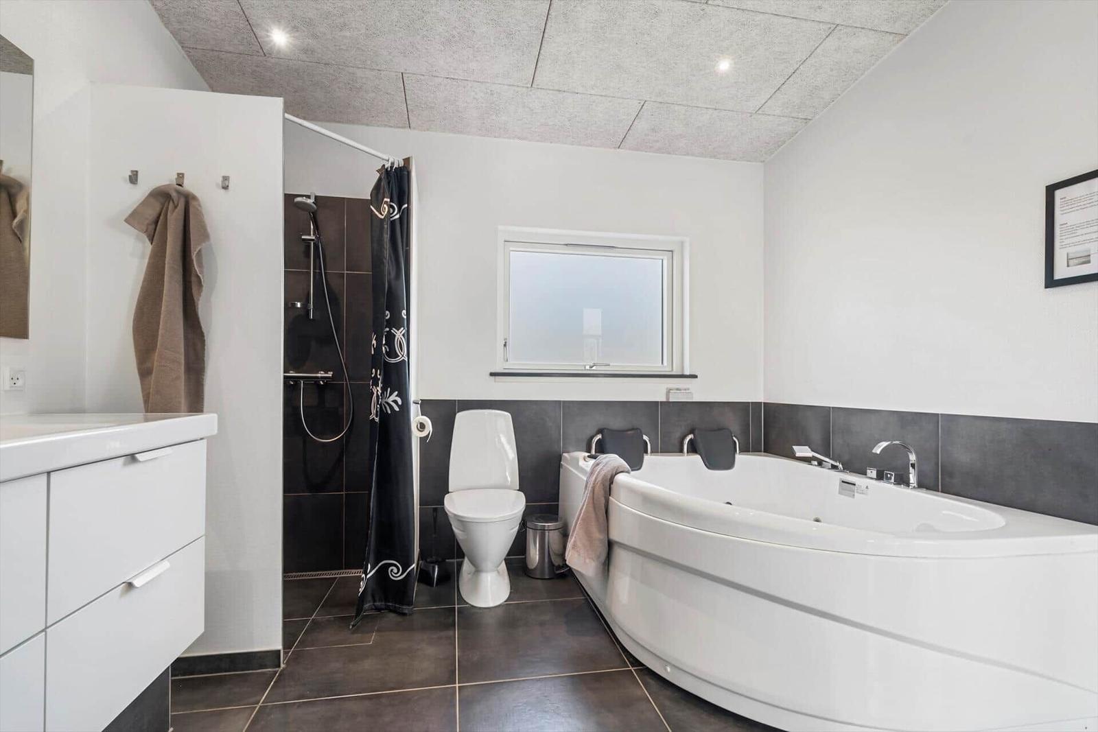 Bathroom with bathtub, shower, and toilet. White walls and dark tiles.
