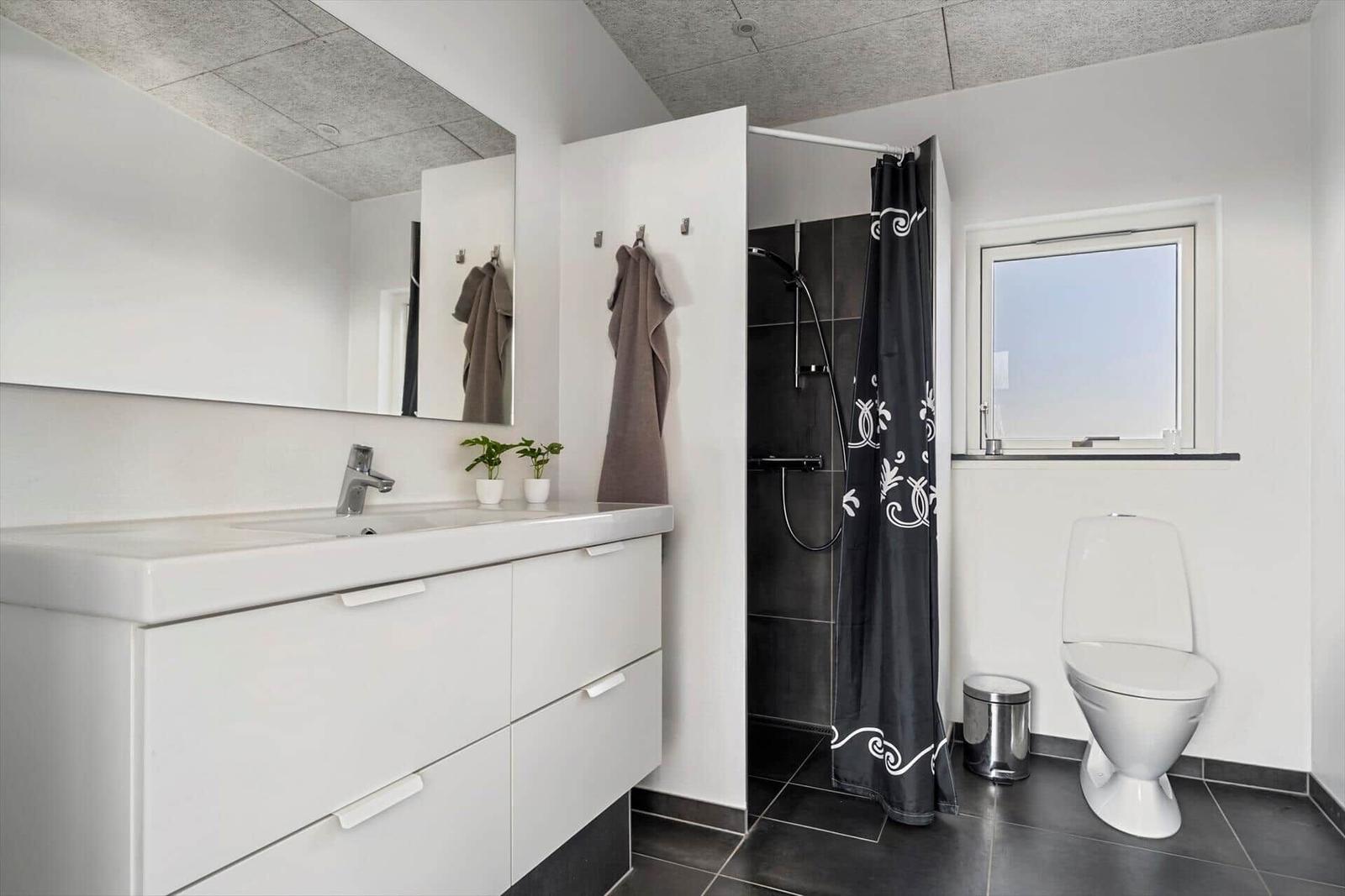 Bathroom with sink, shower, and toilet. Black tiles and white vanity.