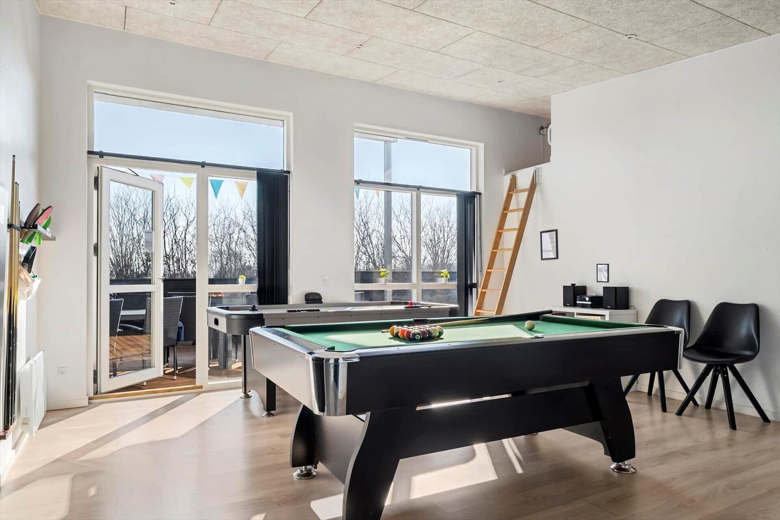 Room with pool table, windows, and terrace door. Wooden floor and black chairs.