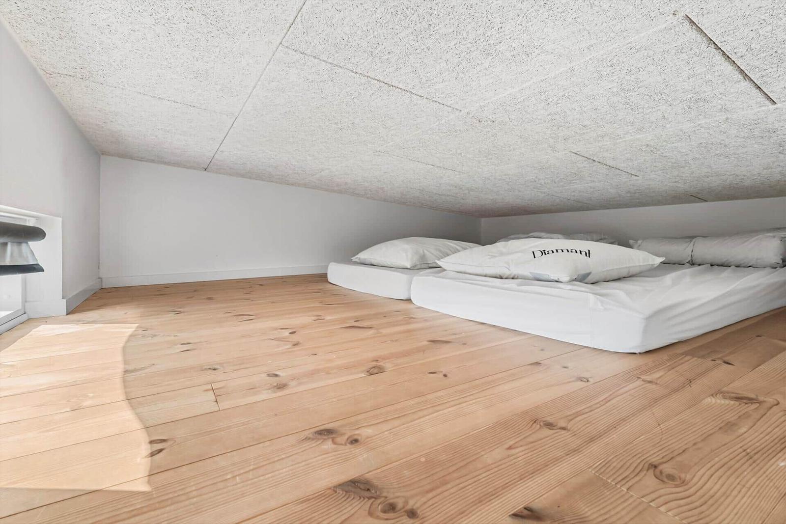 Room with wooden floor and sleeping area under sloped ceiling.