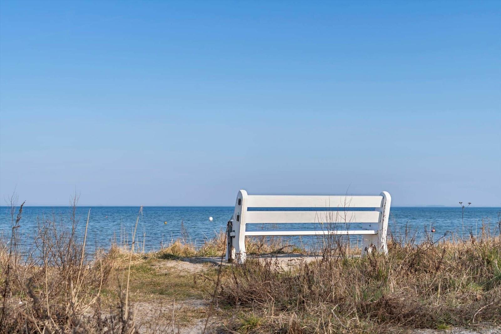 A white bench by the shore with a view of the sea and clear sky.