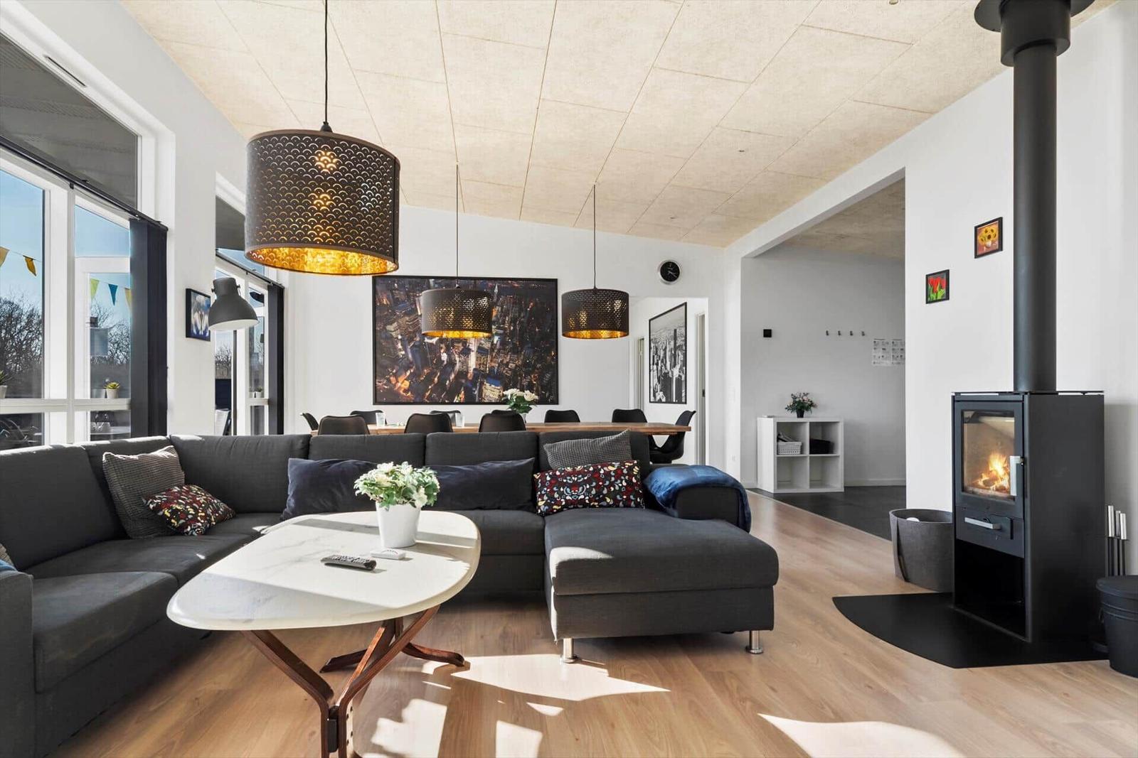 Living room with sofa, table, and wood stove. Large windows and light walls.