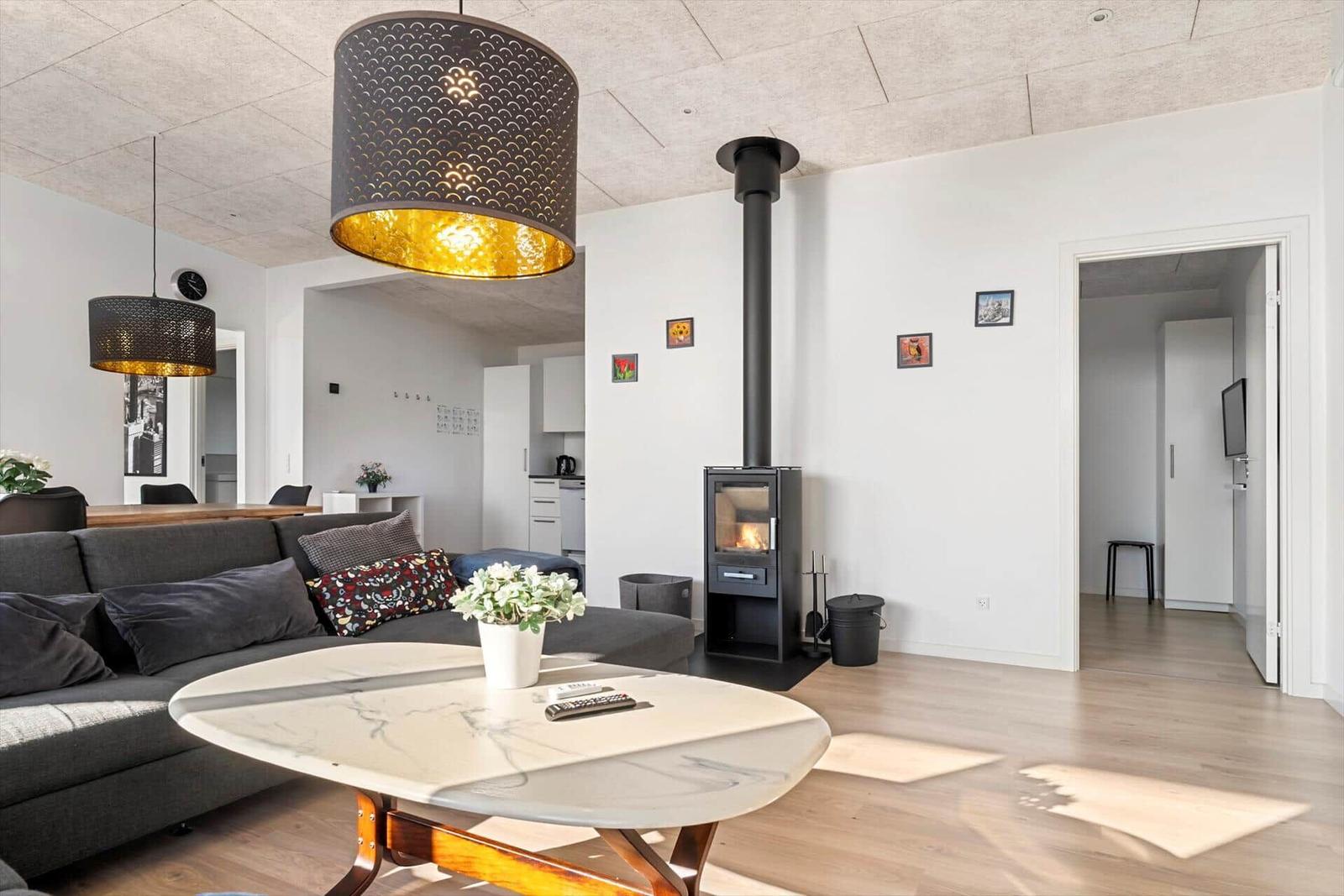 Living room with sofa, dining table, and wood stove. Wooden floor and white walls.