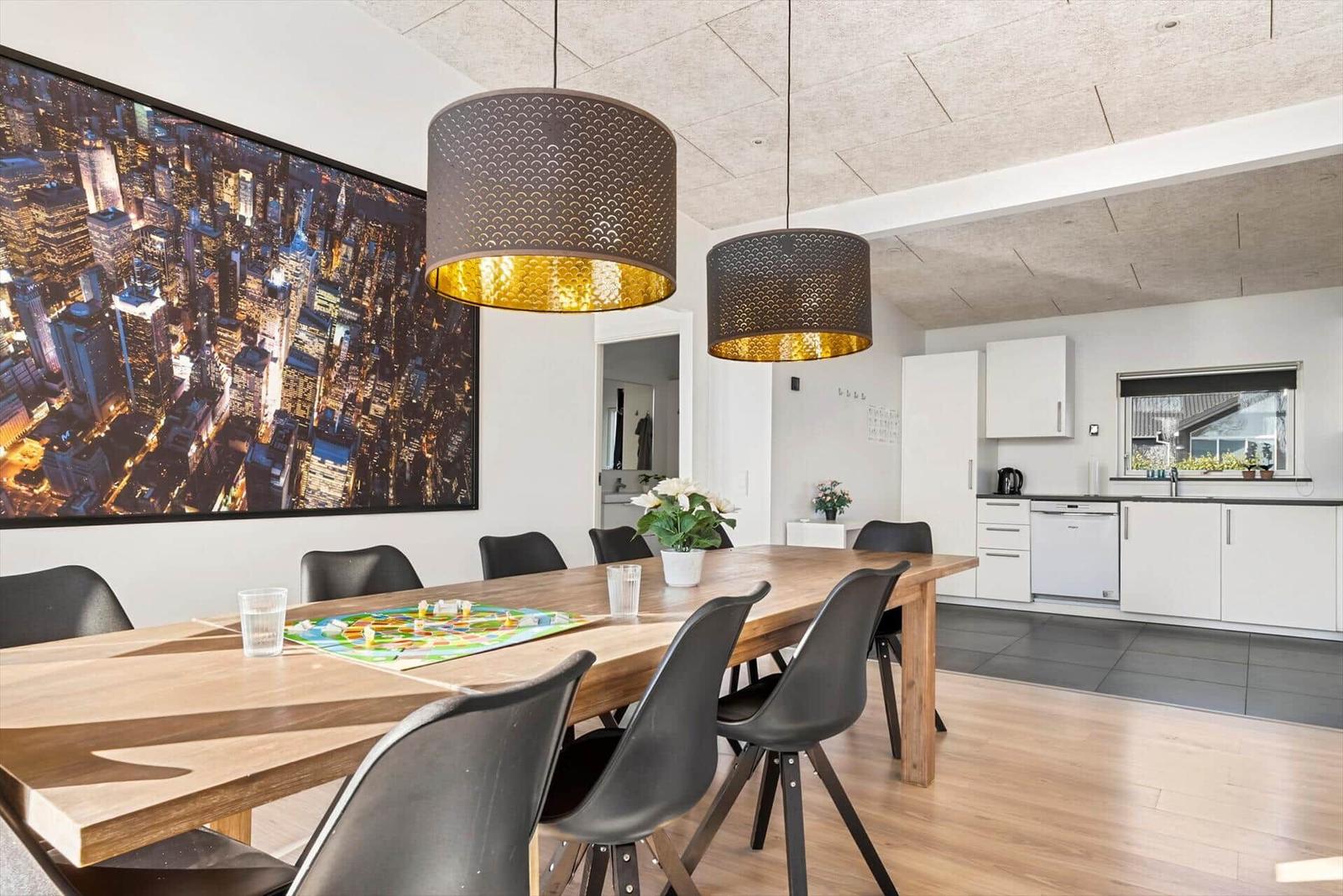 Dining area with wooden table, black chairs, and kitchen area in background.
