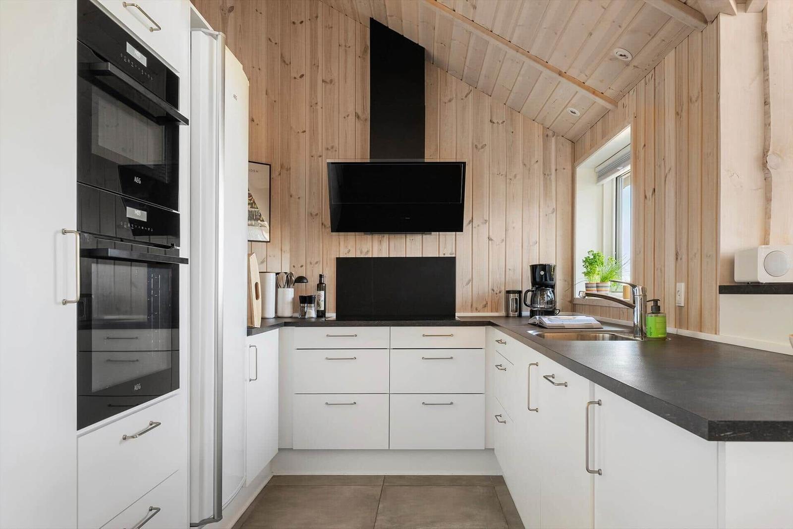 Kitchen with white cabinets, black countertop, and wooden wall cladding.