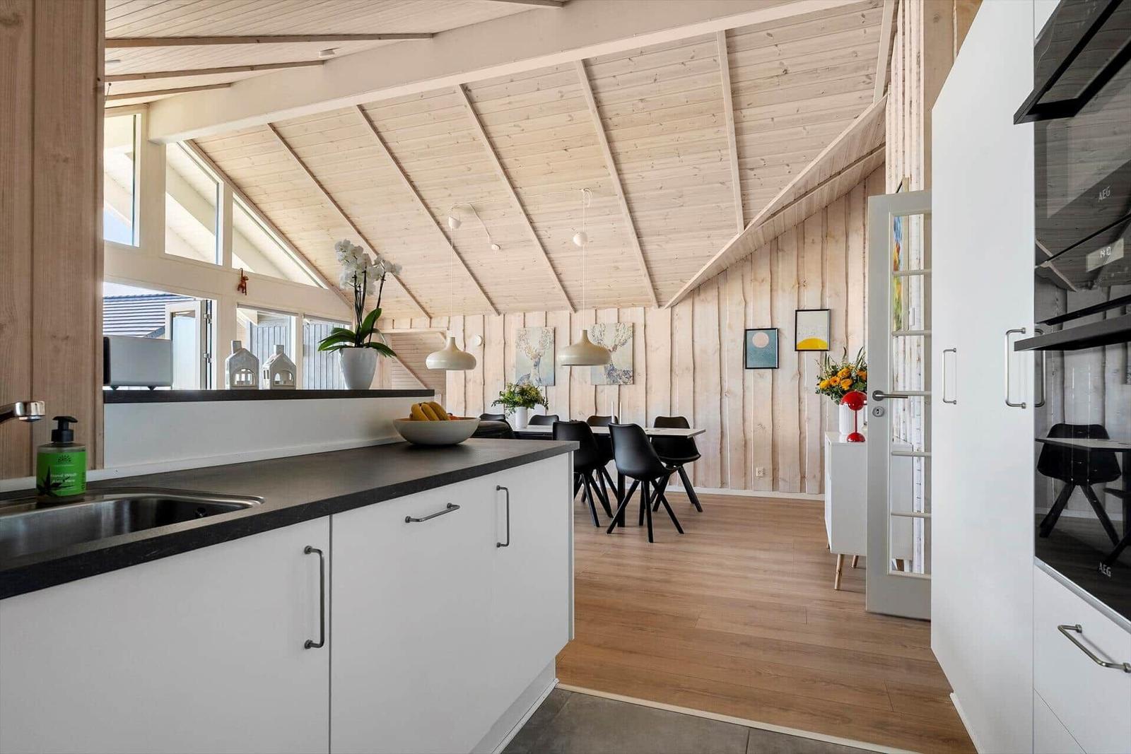 Kitchen with dining area under wooden roof, white cabinets, black countertop, wooden floor, and windows