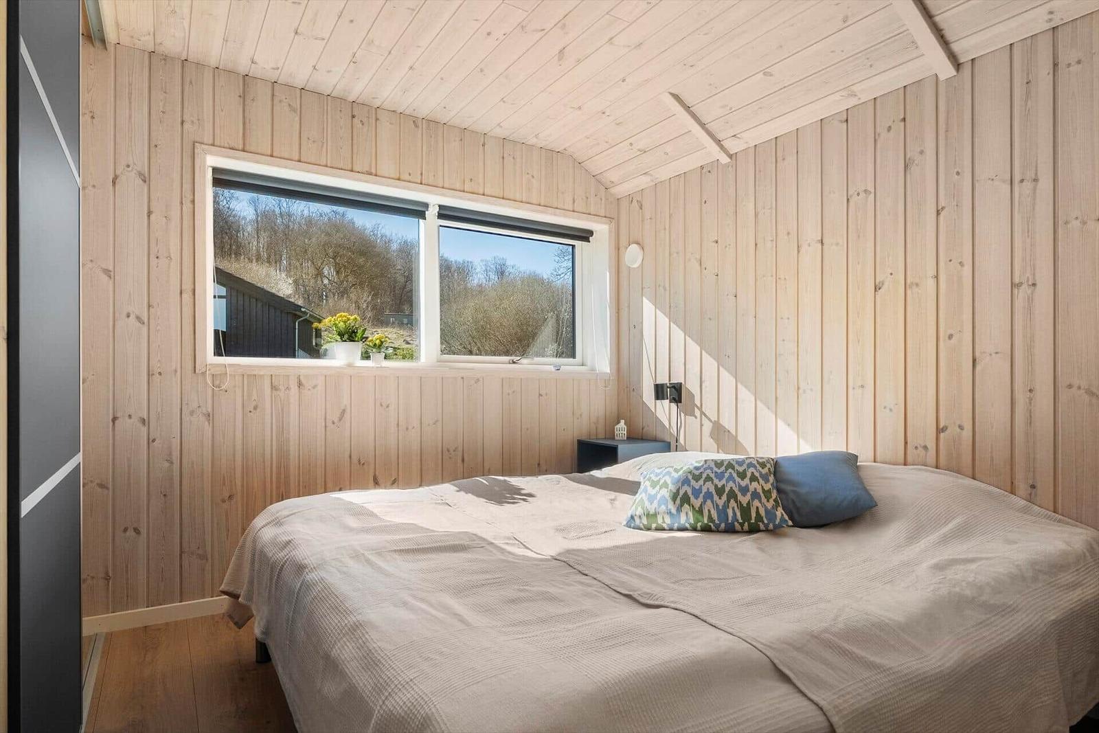 Bedroom with wooden walls and window view of forest.