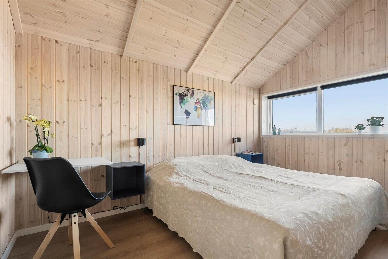 Bedroom with wooden walls, bed, desk, and window.