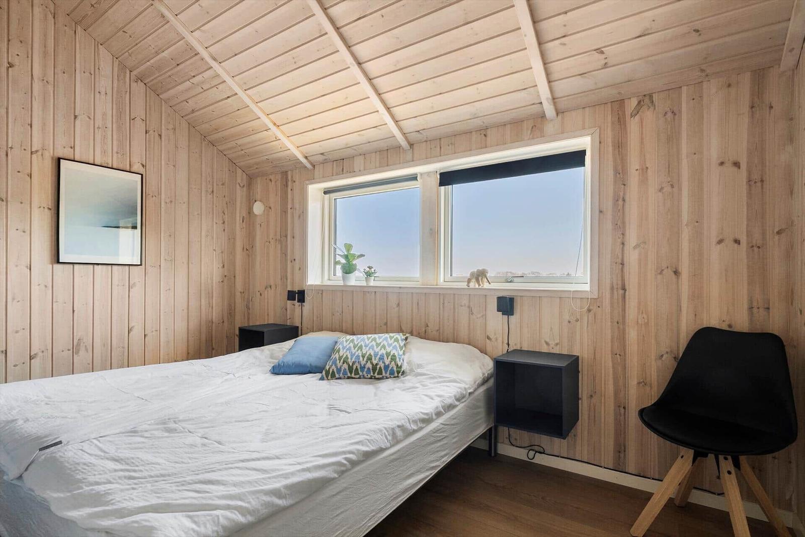 Bedroom with wooden walls, bed, window, and chair