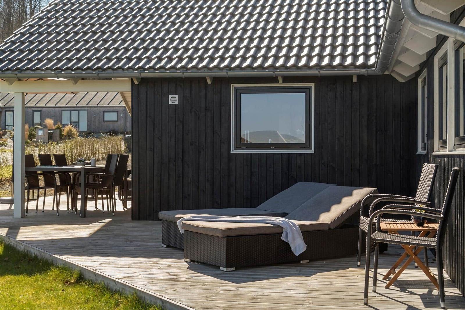 Deck with lounge, table and chairs in front of a house with dark wood siding.