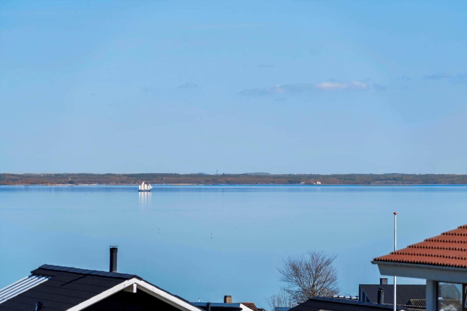 Wide view of calm water with sailboat and vacation house roofs in the foreground.