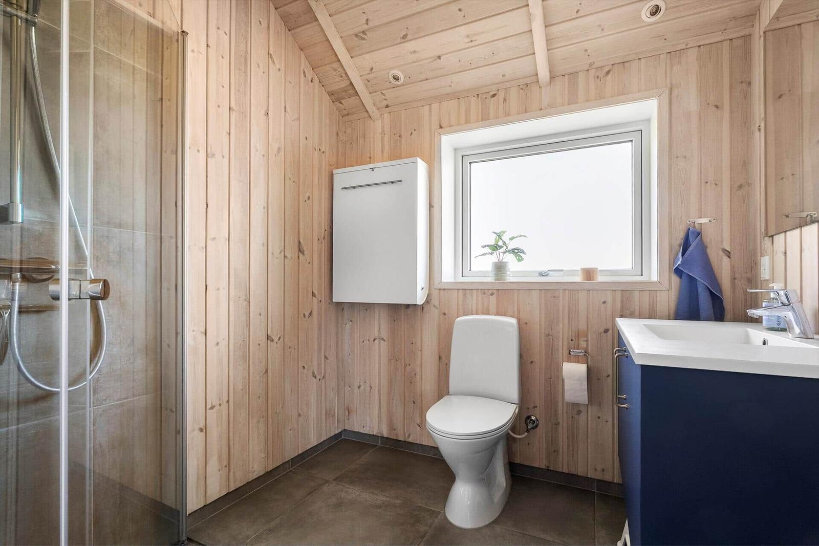 Bathroom with shower, toilet, and sink. Wooden walls and window.