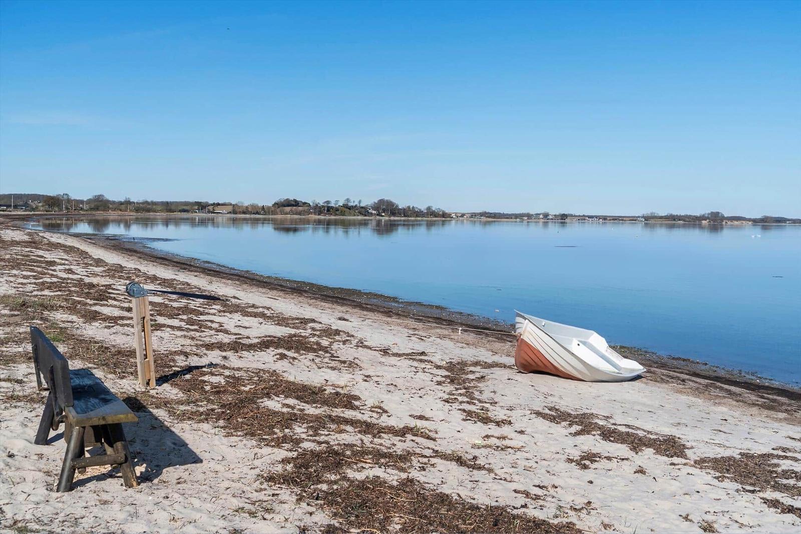 A bench and a boat rest on the shore of a calm body of water.
