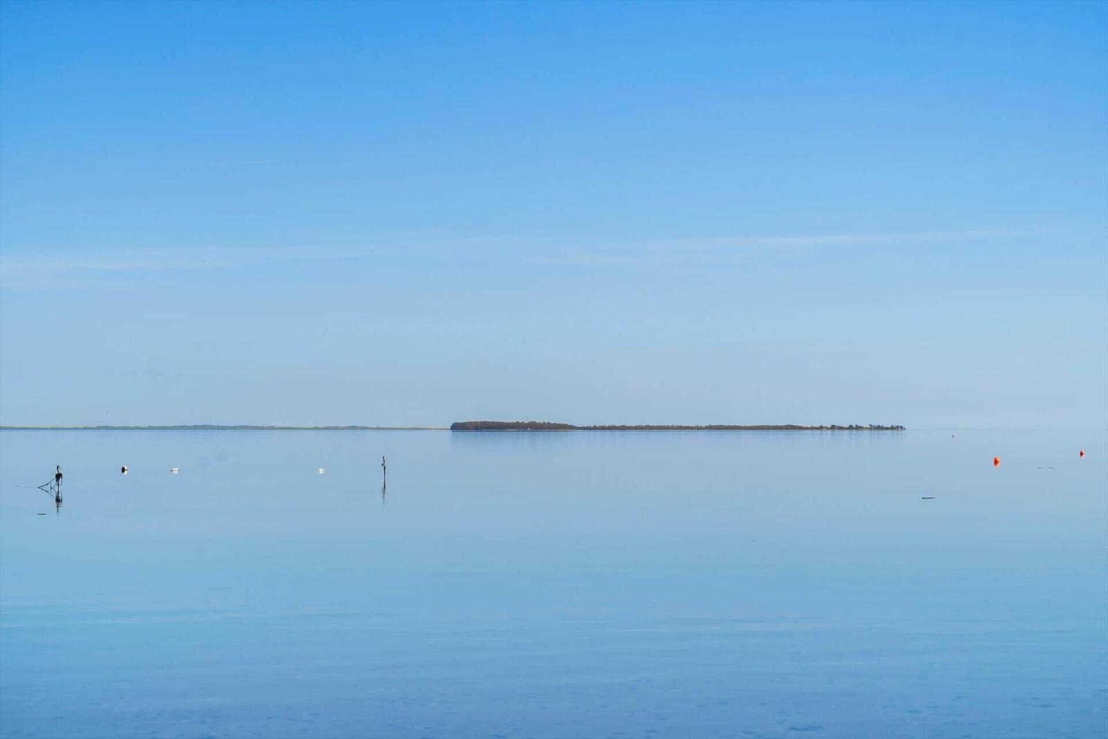 Wide, calm water with an island in the distance and floating markers.