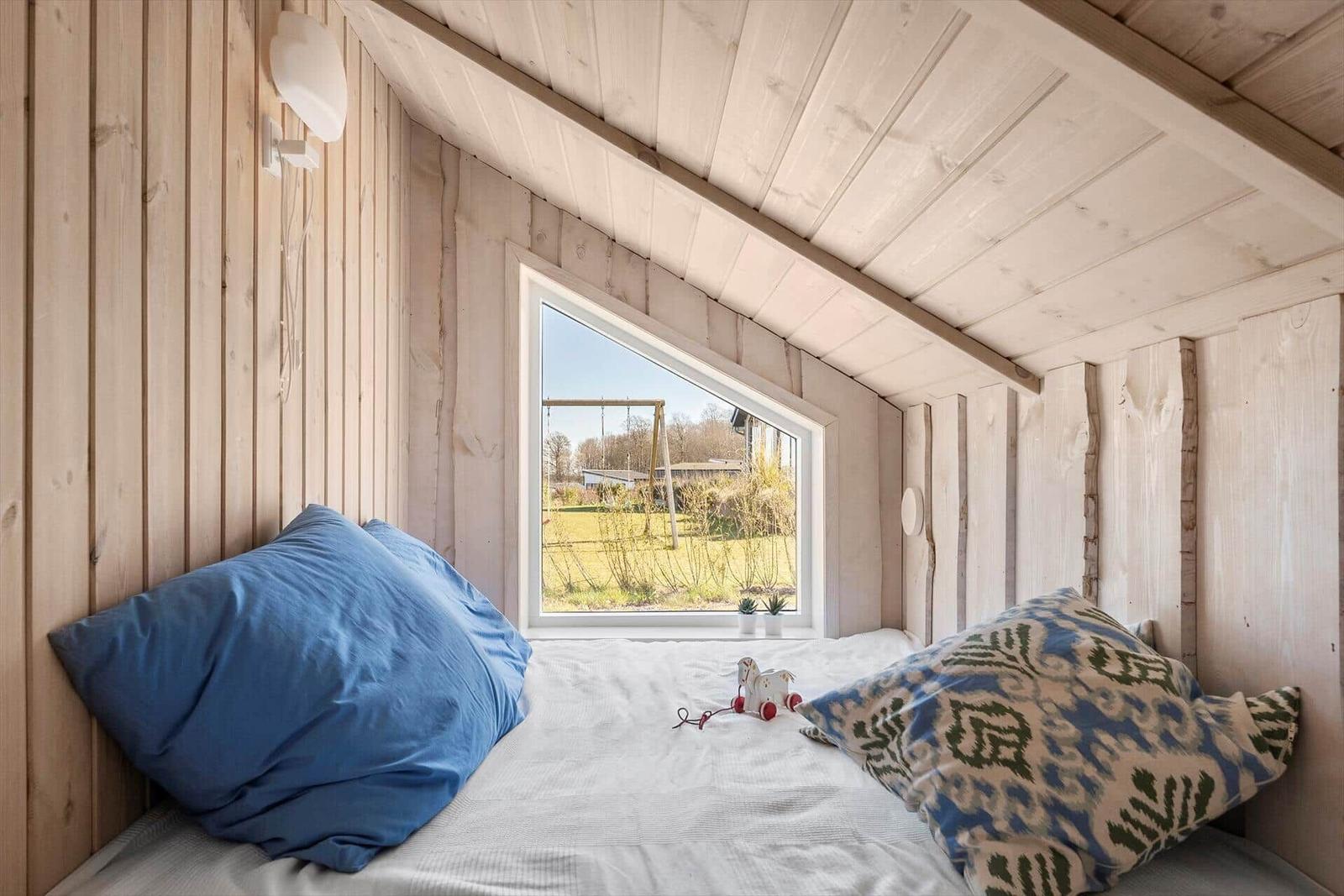 Bedroom with wooden walls and garden view through window.