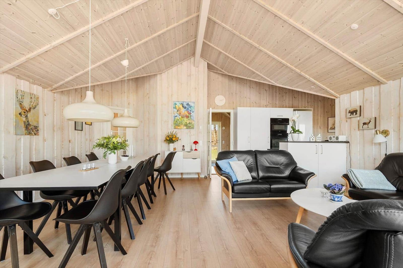 Living and dining area with wooden walls, black seating, and white kitchen unit.