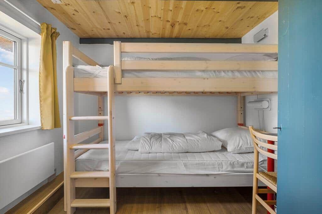 Zimmer mit Holzbett, Fenster und Holzdecke.
