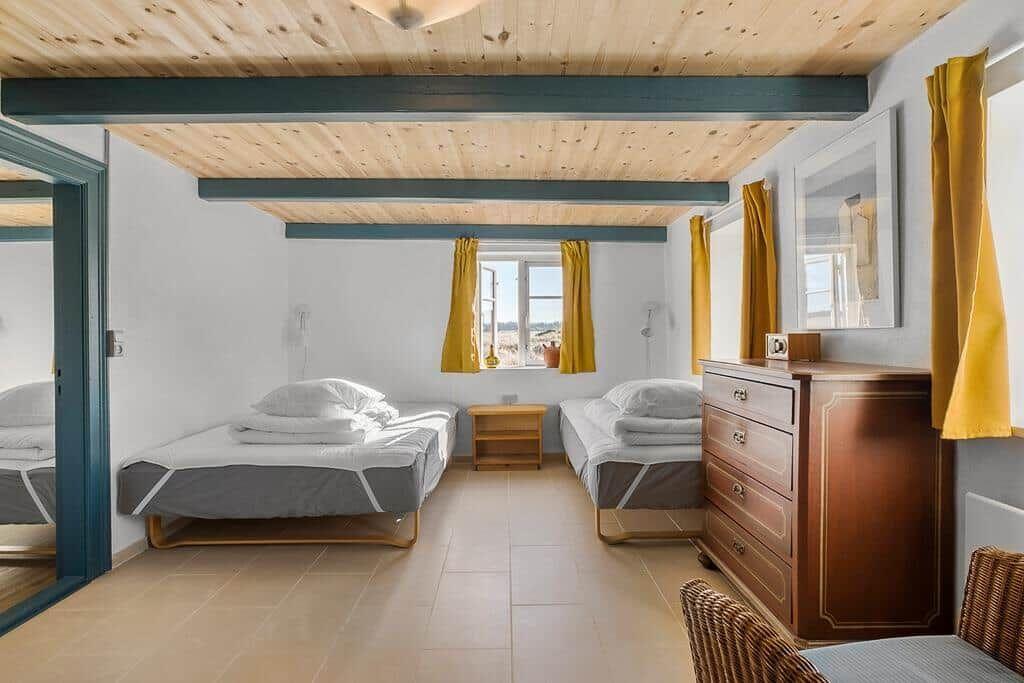 Zwei Betten, Schrank und Fenster mit gelben Vorhängen.
