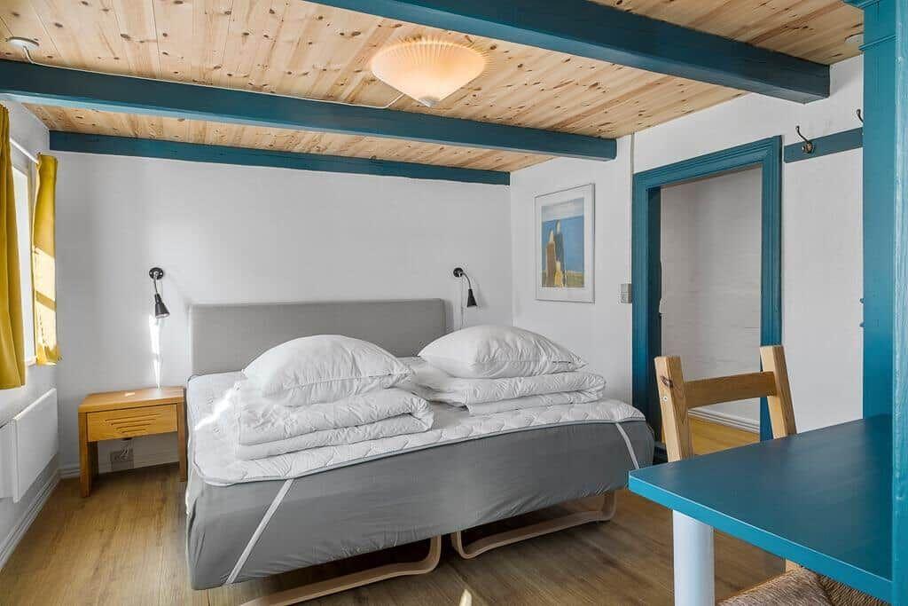 Schlafzimmer mit Bett, Nachttisch und Tisch. Holzdecke mit blauen Balken.
