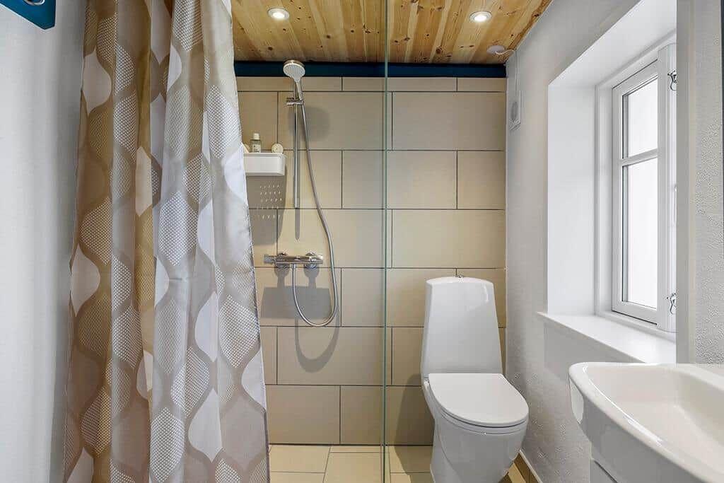 Bad mit Dusche, Toilette und Waschbecken. Holzdecke und Fenster.
