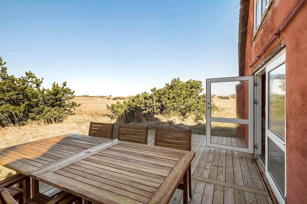 Terrasse mit Holztisch und Stühlen, Blick auf Grasland und Bäume.