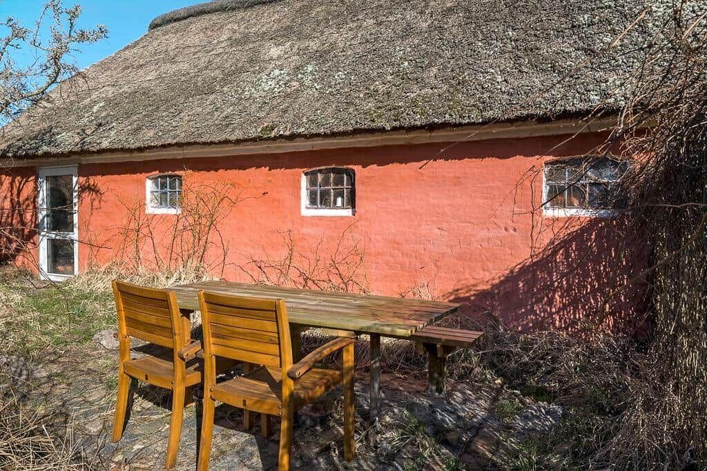 Rotes Haus mit Strohdach und Holztisch mit zwei Stühlen im Freien.