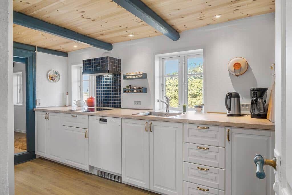 Küche mit weißen Schränken, Holzboden und blauen Balken an der Decke.