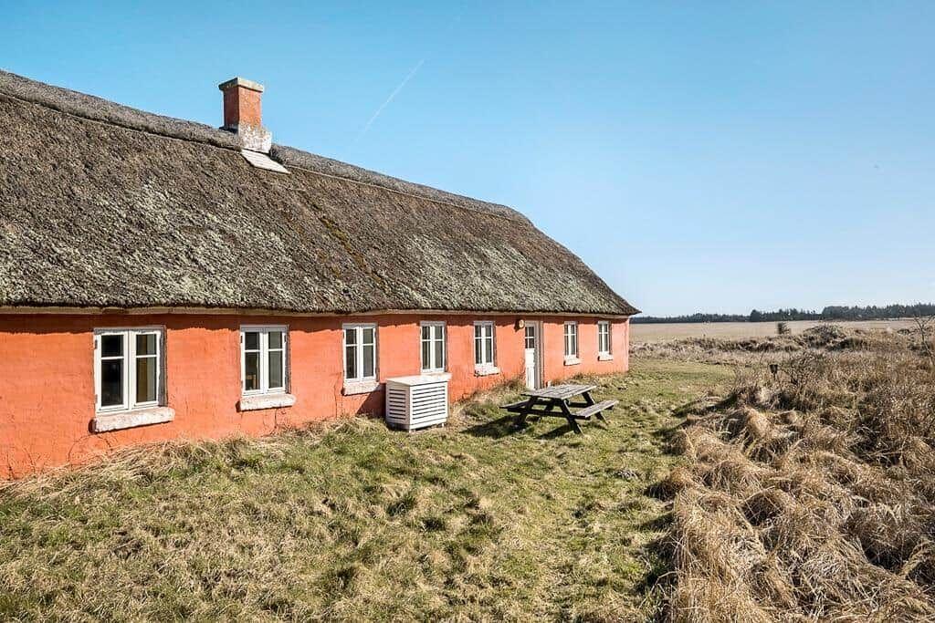 Rotes Haus mit Strohdach, Picknicktisch und Grünfläche.