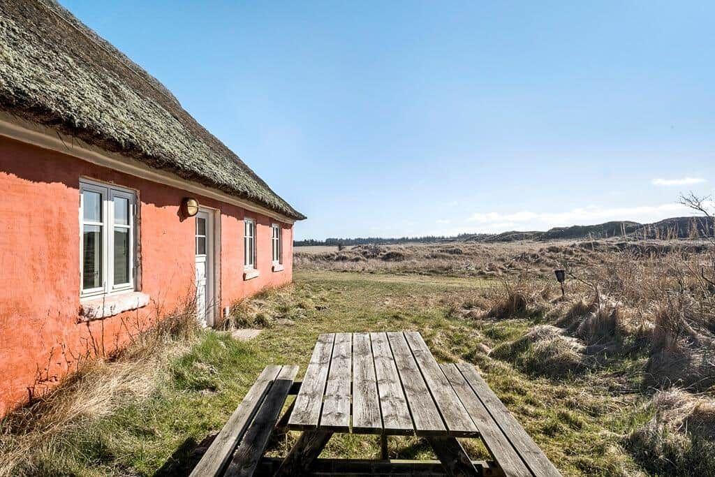 Rotes Haus mit Strohdach und Picknicktisch im Freien.