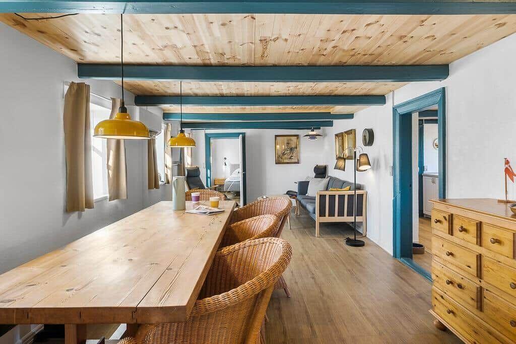 Essbereich mit Holztisch und Stühlen, Wohnzimmer mit Sofa und Kamin, blaue Tür und Holzdecke.